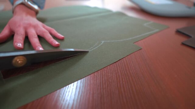Tailor cuts fabric pieces along pattern on worktable. Sewing process in atelier, precision handmade tailoring