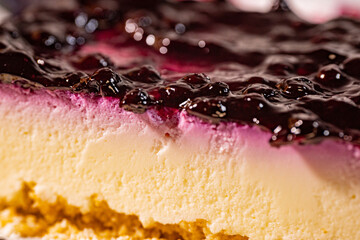 A close-up of a cross-section of a creamy blueberry cheesecake, showing its rich layers—a blueberry topping, a smooth cream cheese filling, and a golden cookie crumb base.