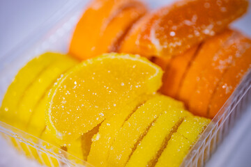 Bright yellow and orange jelly candies in the shape of citrus slices, coated in sugar and neatly packaged in a clear plastic tray. Bright colors and visible sugar texture.