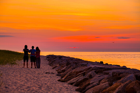 Three teenagers, arm in arm, enjoy the colorful sunrise in Oak Bluffs in Martha's Vineyard