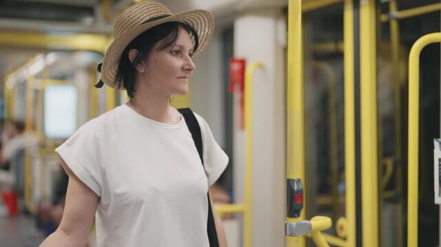 Young pretty fashion woman with hat  traveling by the metro train leaving the underground station. Female stands and looks out of the window, slow motion cinematic shot with selective focus