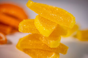 A close-up of stacked pieces of yellow jelly candies covered in sugar crystals with a soft, colorful background.