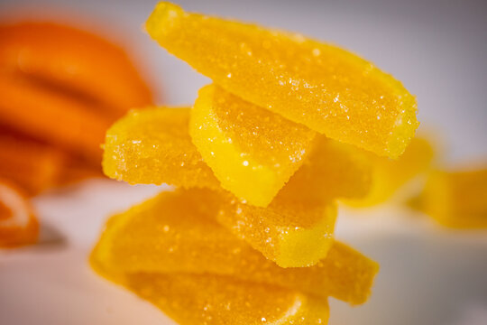 A close-up of stacked pieces of yellow jelly candies covered in sugar crystals with a soft, colorful background.