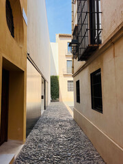 A charming, narrow street in the city center, renovated, with cobblestone paving and barred windows. Malaga, Spain, 2022.