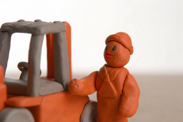Clay worker with forklift model isolated on light background, handmade figure with cheerful expression