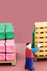 Clay logistics concept with pallets and colorful blocks, miniature figure organizing stacked items in warehouse setting