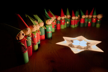 Wichtelfiguren aus Papier als Adventskalender vor einem Sternenteller mit vier Kerzen