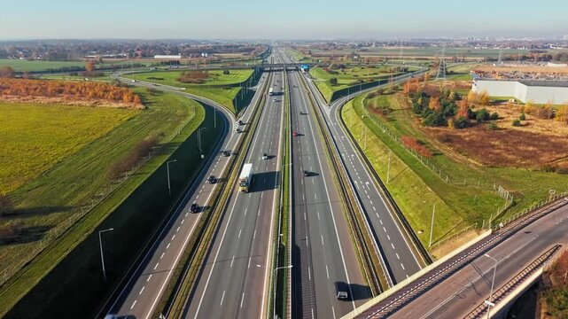 Aerial highway interchange infrastructure transportation road network. High-angle drone view of multi-lane expressway junction with overpasses, vehicles, and countryside landscape on a sunny day