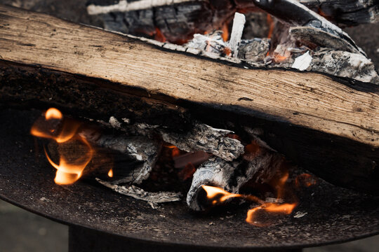 Burning firewood and glowing embers smolder in a metal fire pit, casting warm light and providing heat.