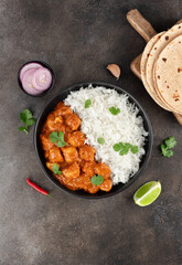 Indian butter chicken with basmati rice, roti, onion, lime and herbs on gray background. Top view