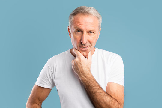 A mature man with grey hair engages in deep thought while touching his chin. He looks directly at the camera with a pensive expression.