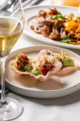 A close-up shot of an elegant appetizer served on pink shrimp crackers with avocado puree and fresh greens, served alongside a glass of sparkling wine in a restaurant setting
