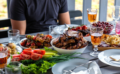 Vegetables and meat are grilled on the table with wine and people. Selective focus.