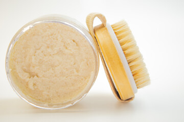 Glass jar filled with creamy body scrub next to a wooden brush, highlighting a soothing skincare experience, perfect for pampering and rejuvenation