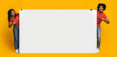 A couple stands happily together, each holding a large blank sign against a vibrant yellow...