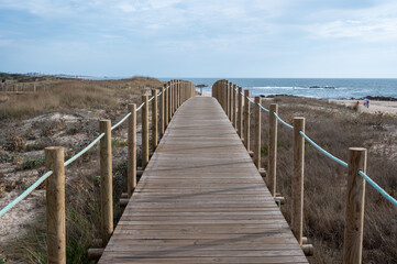 Obraz premium Boardwalk over dunes of Canide Beach on northern coast of Portugal in Vila Nova de Gaia under dramatic autumn cloudscape.