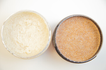Jars of body scrub featuring creamy white and coarse brown textures, placed on a clean surface, highlighting skincare essentials for pampering and self-care routines