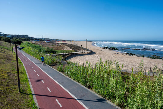 Bicycle, running path and boardwalk along dunes of Canide Beach on northern coast of Portugal in Vila Nova de Gaia under clear blue skies.