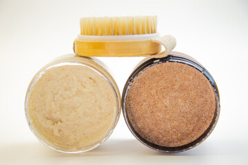 Two jars of body scrubs, one creamy and one coarse, paired with a wooden brush, highlighting natural skincare products for a refreshing and rejuvenating routine