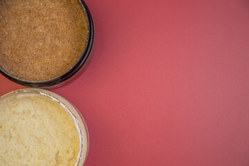 Natural body scrubs in brown and cream jars, arranged on a bright pink background, highlighting organic beauty products with rich textures and inviting colors