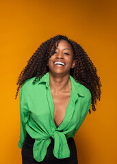 Cheerful Hispanic woman with curly long hair laughing in green shirt on orange studio background