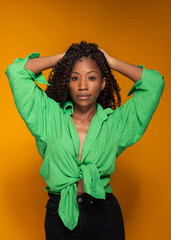 Serious African American woman in green shirt posing with hands on head on orange studio background