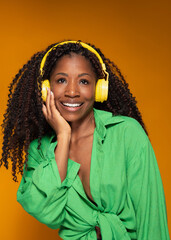 Smiling Hispanic woman in green shirt enjoys music with yellow headphones on yellow background