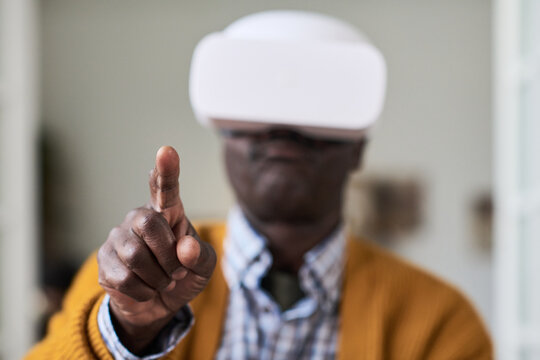 Black mature man wearing virtual reality headset interacting with digital interface, extending finger forward as if touching or selecting something in virtual environment