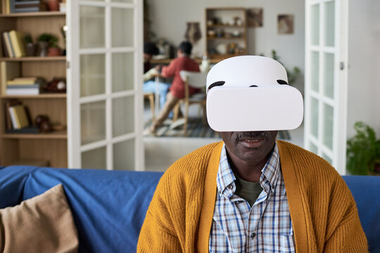 Mature Black man wearing virtual reality headset sitting indoors, interacting with digital content
