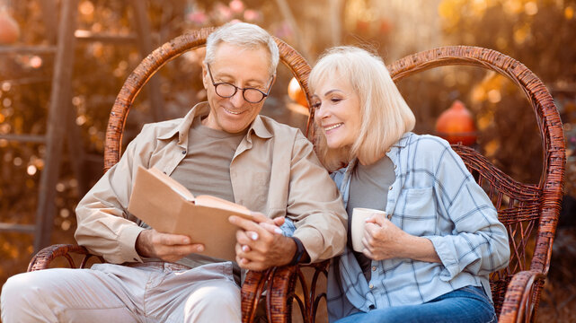 Two people sit closely on a swing chair, sharing a book. They smile at each other as sunlight filters through the trees, creating a warm and inviting atmosphere in the garden.