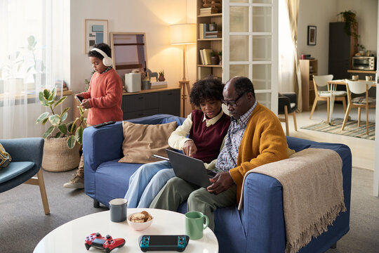 Senior Black man and young boy sitting on sofa using laptop together in modern living room