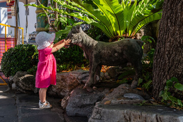 Little girl in a pink dress touching a stone animal sculpture in a park, smiling and exploring with curiosity, happy childhood and learning concept. 