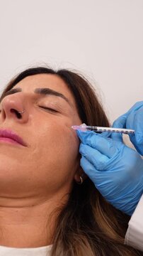 Slow motion close up of a dermatologist performing a facial cosmetic injection on a female patient's face for an anti aging treatment