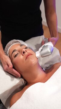 Professional beautician performing non invasive high intensity focused ultrasound facial treatment on a client lying on a beauty couch