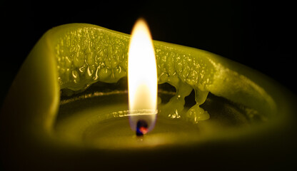 Close-up of burning yellow-green candle with melting wax details and soft flame against dark background