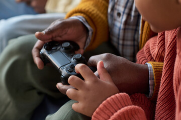 Black child and Black man holding game controller, playing video game together, close up on hands and device, intergenerational bonding, focus on interaction and technology
