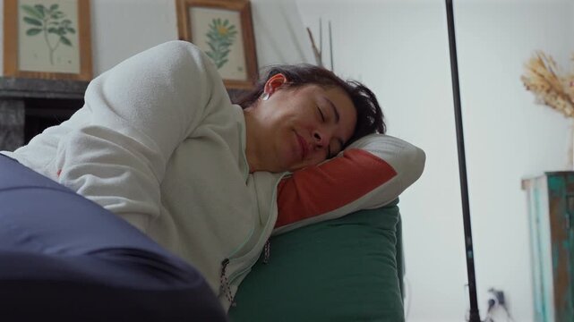 Mother lying on couch yawning widely in soft home light, capturing candid moment of fatigue, rest, and everyday family life with relaxed natural expression during quiet afternoon at home