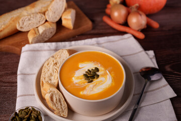 a cozy autumn setting featuring a bowl of creamy pumpkin soup garnished with seeds next to sliced baguette and surrounded by fresh vegetables on a rustic wooden table, setting, artistic, composition
