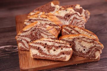 close-up of sliced zebra cake with marbled chocolate and vanilla layers on wooden cutting board against dark wood background, showcasing a deliciously swirled pattern, oven, snack, cake, butter