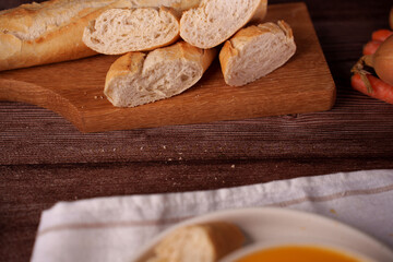 rustic kitchen scene featuring sliced baguette on wooden board, warm soup partially visible near foreground, set on wooden textured table with onions and carrots adding earthy feel, corner, savory