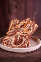 close-up of sliced marble cake arranged on a white ceramic plate against a rich, dark wooden backdrop, showcasing intricate chocolate and vanilla swirls creating a homely, cozy atmosphere, wholesome