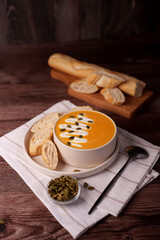 cozy autumn setting with creamy pumpkin soup garnished with pumpkin seeds and cream, accompanied by slices of fresh baguette on wooden surface with warm rustic atmosphere, tabletop, side, fresh