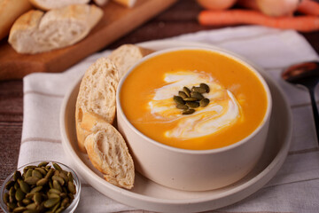 cozy autumnal setting featuring a creamy pumpkin soup garnished with seeds and accompanied by rustic bread slices, evoking warmth and comfort with its rich and vibrant presentation, presentation