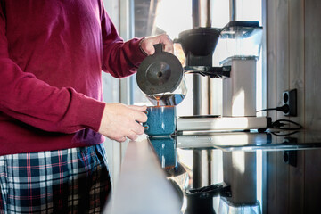 Morning coffee routine as an older man fills a mug in a quiet Nordic kitchen, showing steady movements, familiar habits and a peaceful start of day, with clear copy space for flexible use.