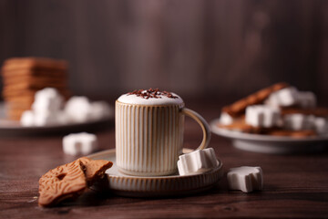 elegant close-up of a stripely textured cup of hot cocoa topped with chocolate sprinkles and surrounded by marshmallows and biscuits on a wooden table setting, decorative, layered, biscuit, interior