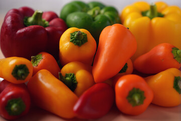 vibrant arrangement of fresh red, yellow, orange, and green bell peppers displaying rich colors and natural textures against a softly lit neutral background, backdrop, colorblock, photograph, macro