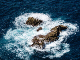 Waves crash against rugged rocks in the deep blue waters of the Bay of Biscay near Gaztelugatxe, Bermeo, Basque Country, Spain, showcasing raw coastal beauty.