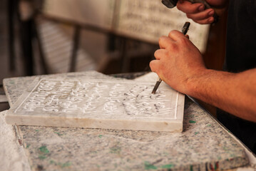 An artisan close up chiseling a stone tablet in the street markets of Fes, Morocco