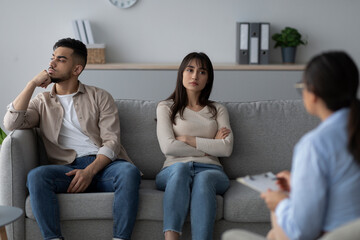 A middle eastern couple sits on a couch in a therapist's office. Both look unhappy and are discussing their relationship problems with a psychologist. They appear to be struggling with communication.