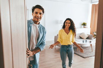 Two friends are happily welcoming each other at the entrance of a well-lit apartment. The modern space features a comfortable living area with soft furnishings and bright colors.